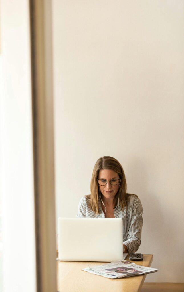 Businesswoman working remotely on a laptop at home, enjoying natural light in a modern, minimalist setting.